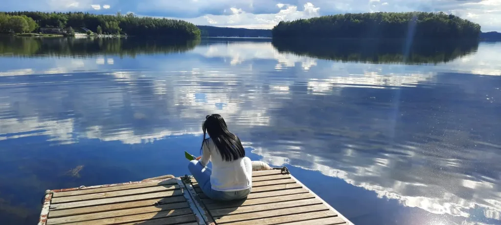 Woman sitting on a jetty by a mirror-smooth lake