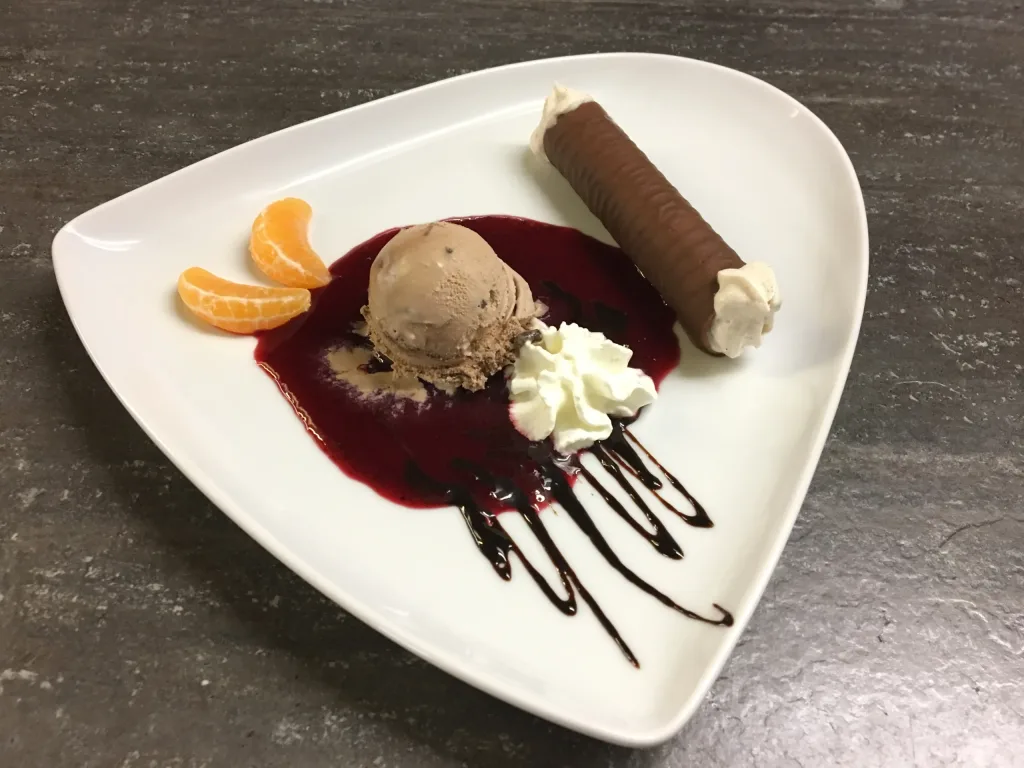 Dessert with ice cream, chocolate rolls and cream on a fruit coulis