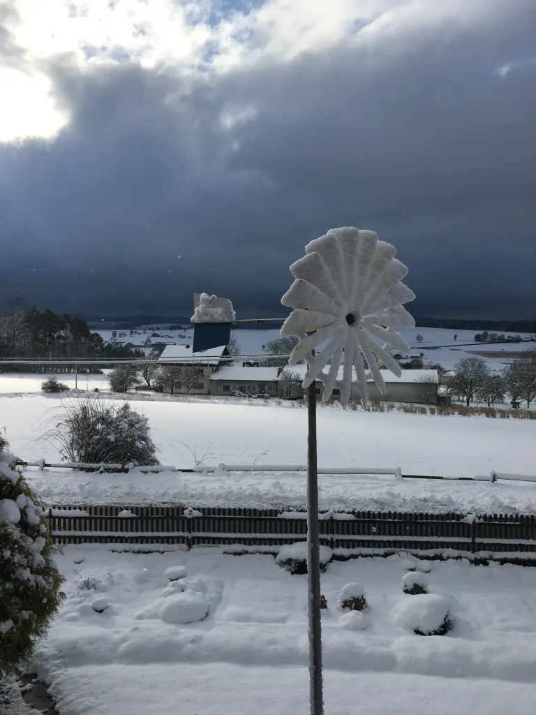 Wind wheel in the snow-covered garden against dark clouds