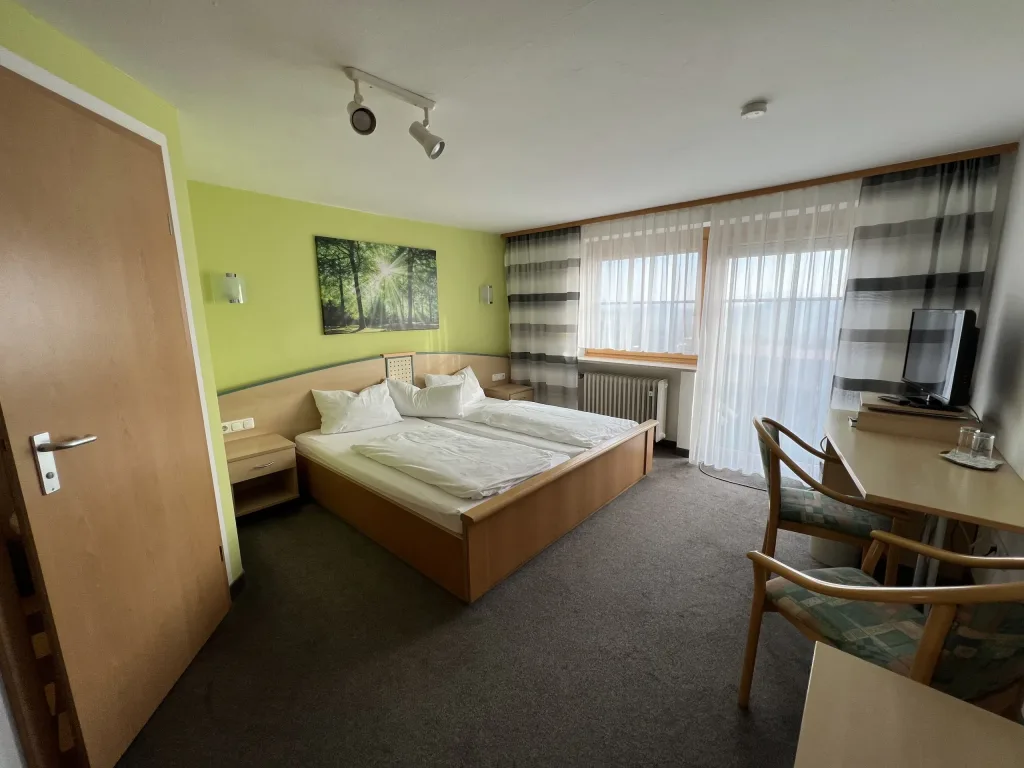 Bright double room with a desk, television and balcony door