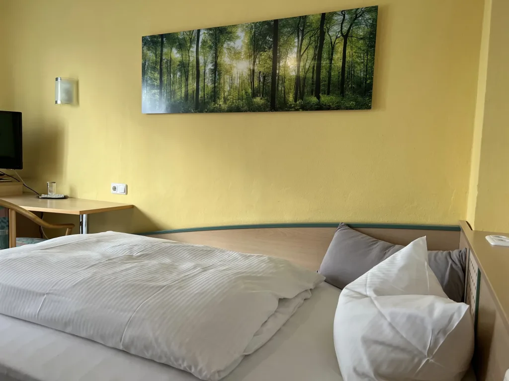 Bed beneath a picture of a forest on a yellow wall