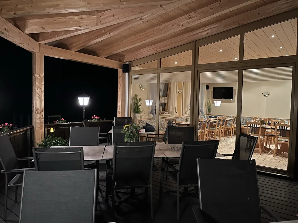 Covered terrace in the evening with a view into the lit dining room