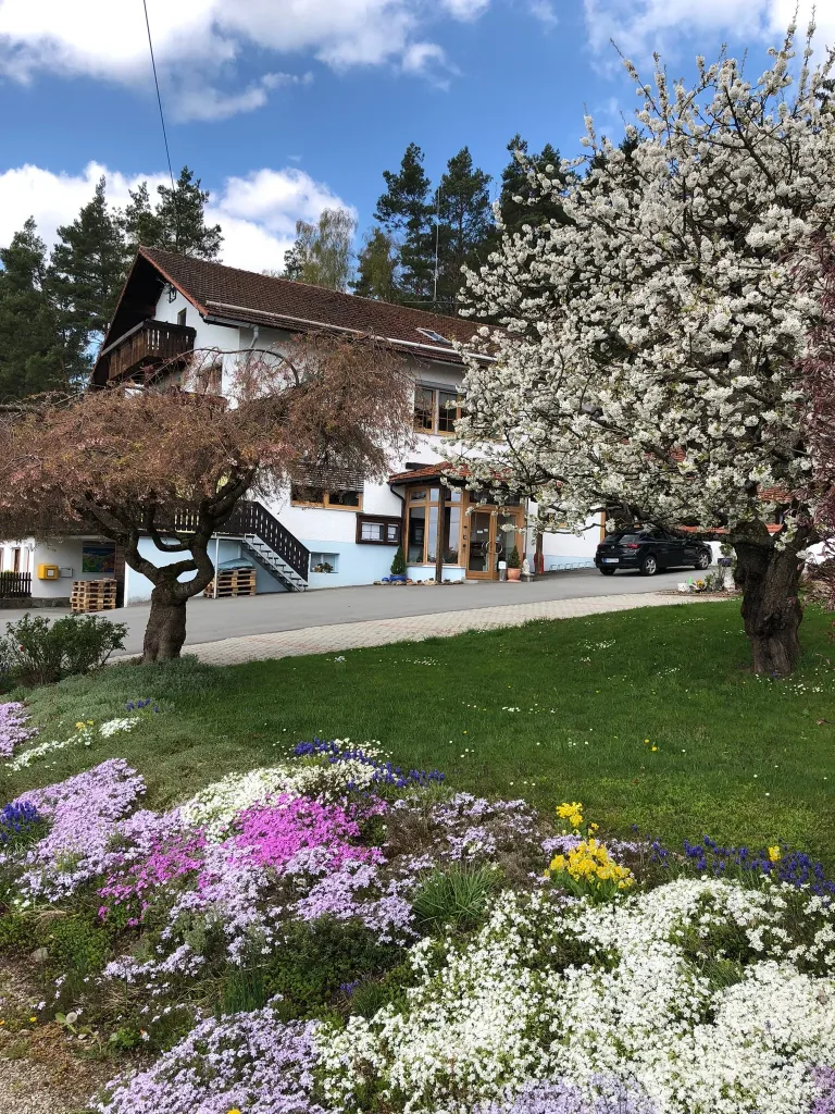 Landhotel Waldesruh behind blossoming trees and flower beds