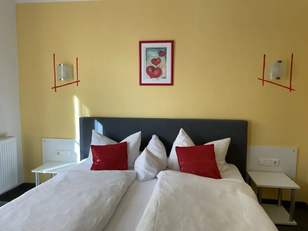 Double room with white bed linen and red cushions against a yellow wall